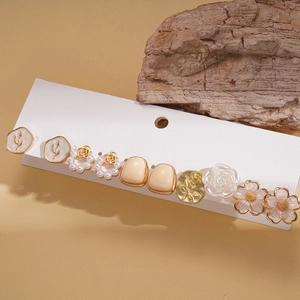 7-pair floral resin and pearl earring set in gold and cream tones on wood decor