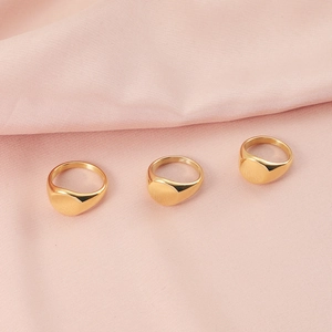 Three gold minimalist oval signet rings displayed on pink folded fabric background