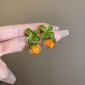 Detail shot of orange persimmon and green leaf stud earrings with glossy resin texture