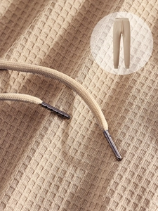 Close-up of beige waffle knit fabric and drawstring with metal tips on casual pants