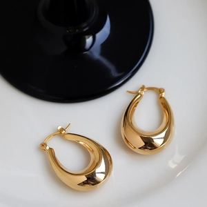 Detailed close-up of polished gold oval hoop earrings on a minimalist decorative plate
