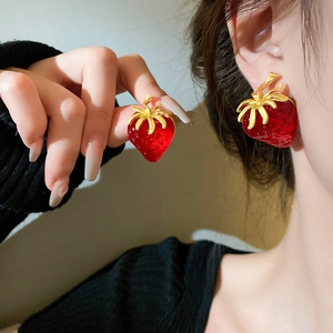 Detailed view of red strawberry earrings with gold leaf accents worn by a model