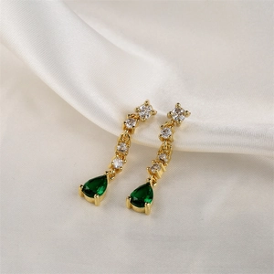 Détail de boucles d'oreilles épingle à nourrice dorées avec gemme verte et zircons blancs