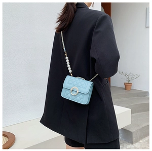 Detail of light blue quilted crossbody bag with pearl strap worn by model on white stairs