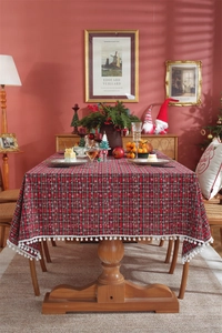 Close-up of red plaid Christmas tablecloth with white snowflakes and pom-pom fringe edge