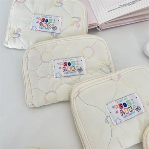 Close-up of quilted cream cotton wallets featuring colorful flower and bow embroidery