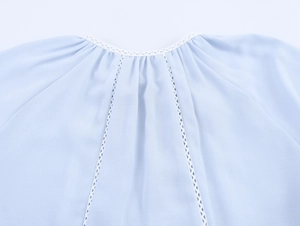 Macro view of light blue blouse with round neck, lace trim, and pleated details
