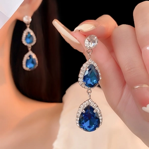 Close-up of blue teardrop crystal earrings with silver needles and shimmering pavé accents
