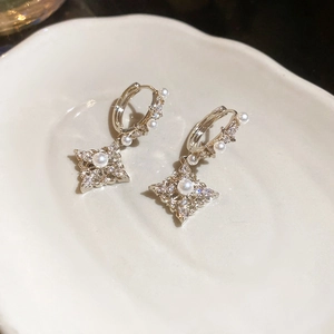 Detail of 18K gold plated zircon star earring with white pearl on ceramic surface