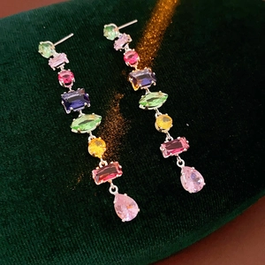 Macro view of long drop earrings with colorful zircons on green velvet background