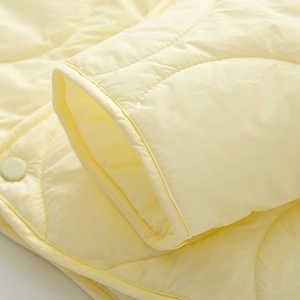 Close-up of diamond quilted yellow padded jacket showing snap buttons and elastic cuffs