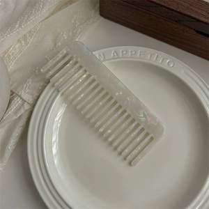 Detailed view of large white pearlescent acetate wide-tooth comb on ceramic dish