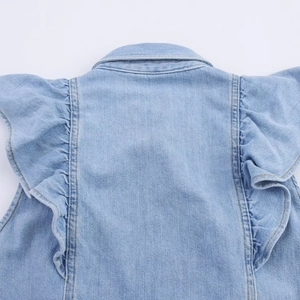 Detail van lichtblauw denim vest met ruches aan de mouwen en gele stiksels als accent