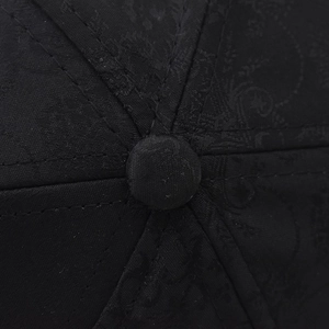 Macro detail of black cotton baseball cap showing paisley jacquard texture and reinforced stitching