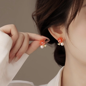 Détail de boucles d'oreilles fleur aux pétales orange et perles portées par un mannequin