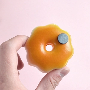 Realistic orange glazed donut magnet for fridge decoration held in hand against pink background