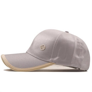 Detail of grey satin baseball cap with metallic M logo and beige contrast brim piping