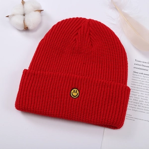 Primer plano del bordado de cara sonriente amarilla en un gorro de punto rojo de invierno