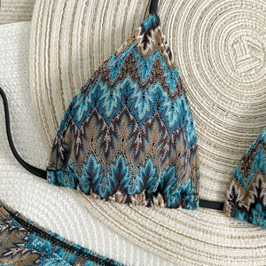 Détail d'un bikini en crochet à motif zigzag aux tons terre sur un chapeau de paille