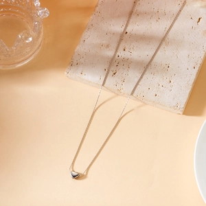Close-up of a minimalist 18K gold titanium steel necklace with a heart pendant on travertine