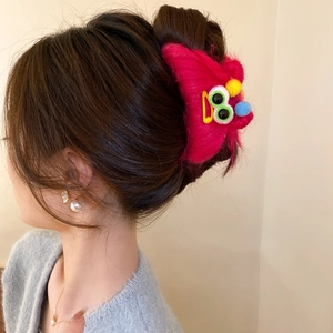 Pink plush monster hair claw clip with colorful eyes shown on a model's hair style
