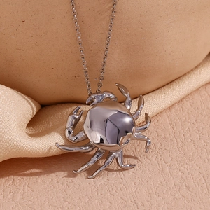Detail of silver crab pendant necklace resting on beige textured fabric in soft lighting
