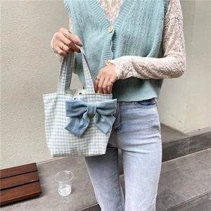 Close-up of a blue plaid handbag with a large denim bow held by a model in casual outfit
