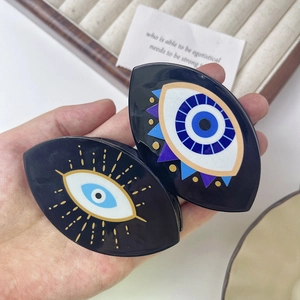 Hand holding evil eye pattern hair claw clips in blue and black acetate finish