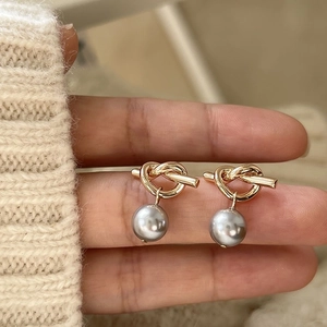 Close-up of golden knot stud earring with a polished grey pearl on white knitwear