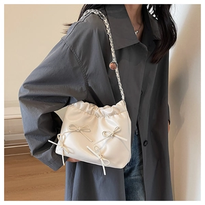 Detail of white pleated bucket bag with bow accents and metallic chain strap on model