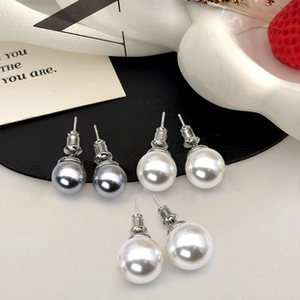 Detail view of round white and grey pearl earrings on white silk with a card