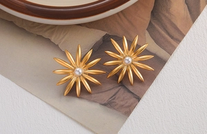 Detailed view of golden sunflower earrings with pearl center on artistic background