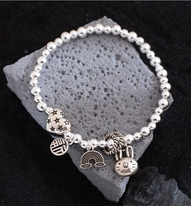 Detailed close-up of beaded bracelet with rabbit, heart, and fortune charms on stone