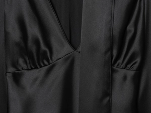 Detailed view of black satin blouse featuring elegant pleated texture and a deep V-neckline