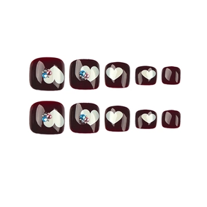 Dark cherry red press-on toenails with white heart patterns and colorful rhinestones