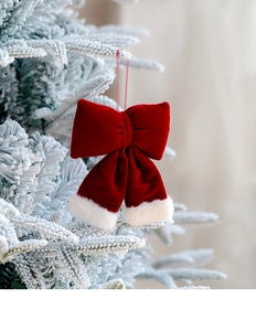 Close-up of red velvet Christmas bow with faux fur trim hanging on a snowy pine branch