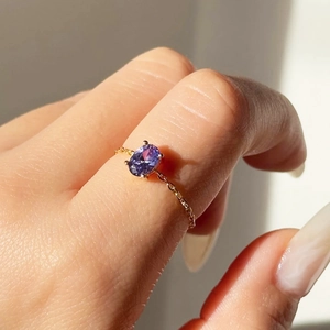 Close-up of a gold-plated chain ring featuring an oval purple zircon on a model finger