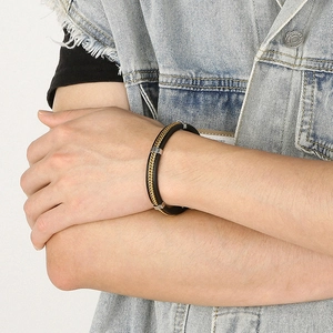 Detail of men's black braided leather bracelet with gold dragon-scale steel chain
