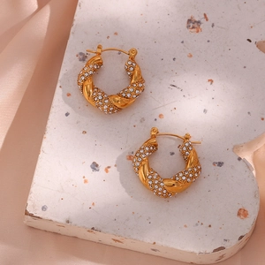 Detailed macro view of gold-plated twisted hoop earrings with micro-paved zircons on stone