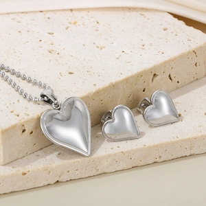 Polished silver heart jewelry set with pendant necklace and stud earrings on stone base