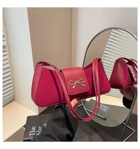 Deep red bow baguette bag held against a round mirror in a cozy indoor setting