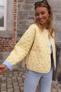 Detail of light yellow quilted jacket featuring contrast piping and blue striped sleeve lining