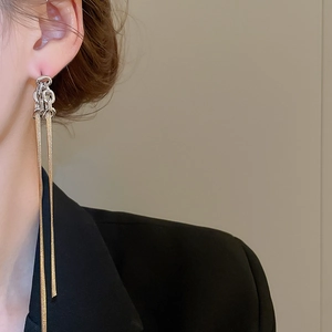 Détail macro de boucles d'oreilles à longs pompons en chaîne serpent dorée sur modèle