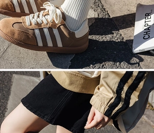 Detailed view of brown suede sneakers with white stripes and casual lettered mid-tube socks