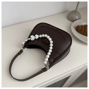 Close-up of heart embossed texture and pearl charm chain on a brown crescent shoulder bag
