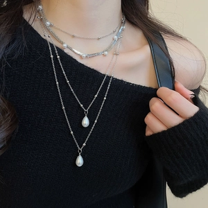 Detail of multi-layered silver necklace featuring teardrop pearl pendants on a model