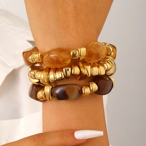 Close-up of stacked bohemian gold metal bracelets with amber and marble resin beads