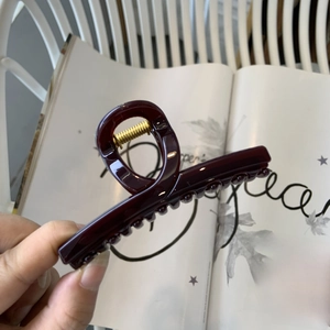 Détail d'une pince à cheveux en résine rouge vin avec ressort doré pour femmes