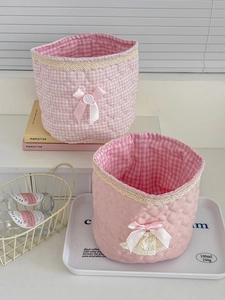 Detail of pink quilted lace storage baskets with ribbon bows and plaid lining for desk