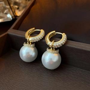 Detail of gold zircon earrings featuring large round pearls on dark jewelry box background